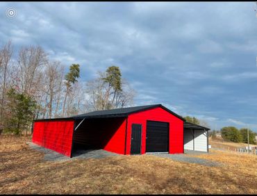 Red and gray metal garage with black roof in a rural area under a cloudy sky.