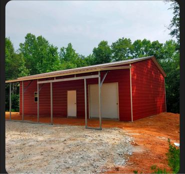 A red metal barn with white doors and an attached metal frame canopy.