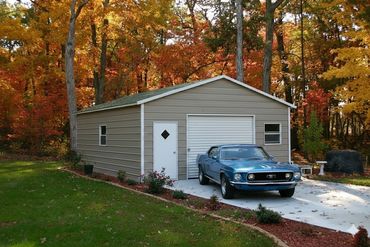 Blue classic car parked on driveway in front of a beige garage with autumn trees.