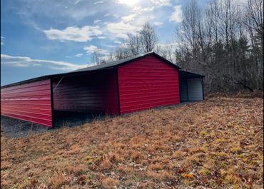 Large red metal shed in a rural autumn field under a partly cloudy sky.