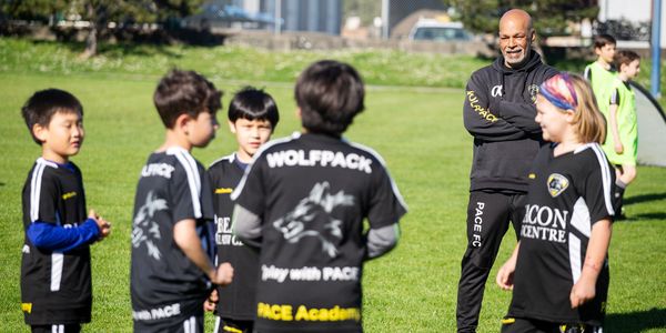 A coach talks to young soccer players on a sunny field.