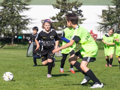 Children playing soccer on a sunny day in bright uniforms.