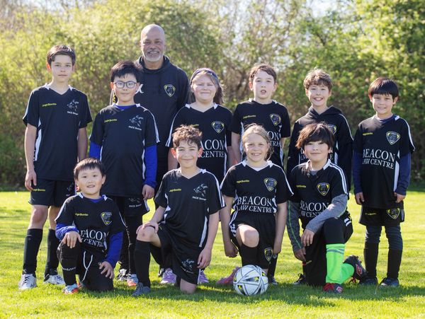 Youth soccer team posing outdoors with their coach on a sunny day.
