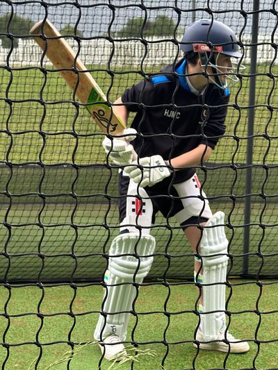 a boy in full cricket equipment about to his a shot during a 1-2-1 session. 