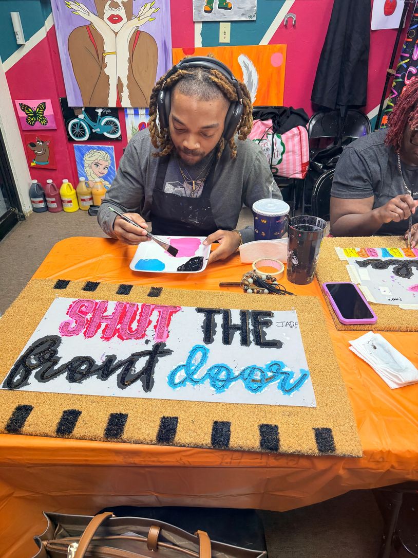 Man painting a colorful sign that says 'SHUT THE front door' at a vibrant art studio.