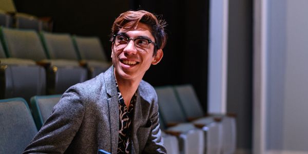Young man smiling while sitting in a theater or auditorium.