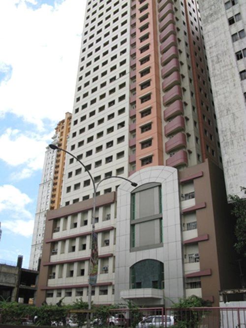 Tall residential building with pink and white exterior under a cloudy sky.