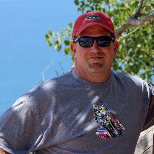 Man in red hat and sunglasses smiling in front of water and trees