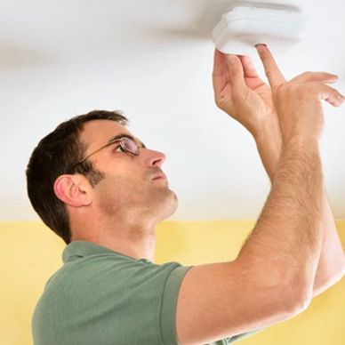 Man installing or testing a smoke detector on the ceiling.