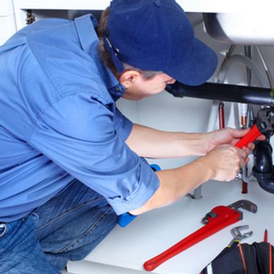 A plumber repairing pipes under a sink with tools.