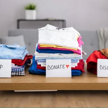 Stacks of clothes sorted for donation, donation, and discard on a table.