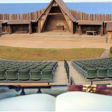 Outdoor theater with wooden stage and rows of green seats facing the water.