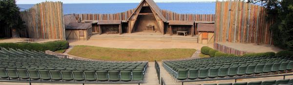 Outdoor theater with wooden stage and ocean backdrop.