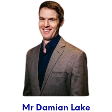 Mr Lake side shot, smiling, wearing a taupe jacket and blue shirt. 