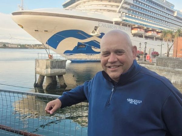 A man smiling near a docked cruise ship named Caribbean Princess.