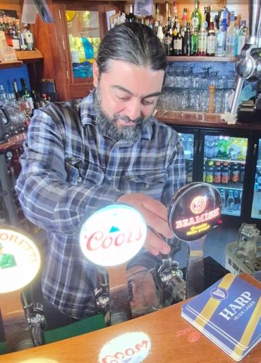 Bartender serving beer from taps in a cozy bar setting.
