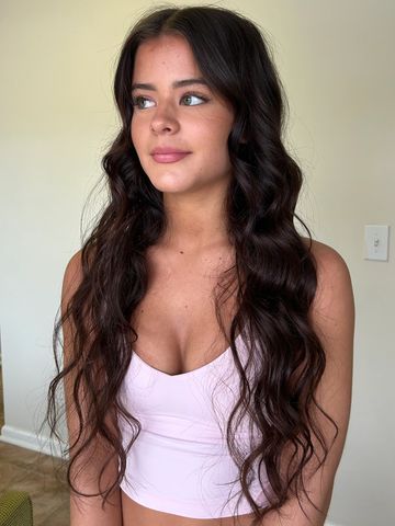 Young woman with long wavy dark hair wearing a light pink top.