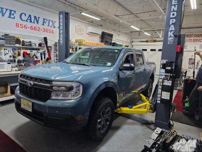 Blue pickup truck in a mechanic shop on a lift.