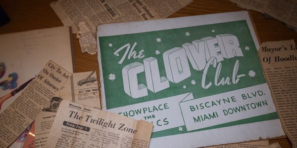 Black and white newspaper articles plus a Clover Club cardboard photo holder.