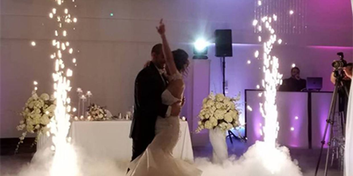 Bride and groom share a romantic dance amid sparkling fireworks and fog effects at their wedding.