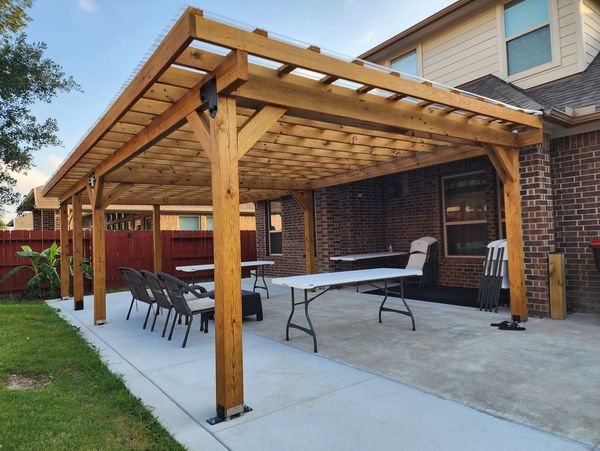 A newly constructed wooden pergola over a stamped concrete patio with outdoor dining furniture and chairs, providing a shaded outdoor living space in a backyard in Sugar Land, Texas.