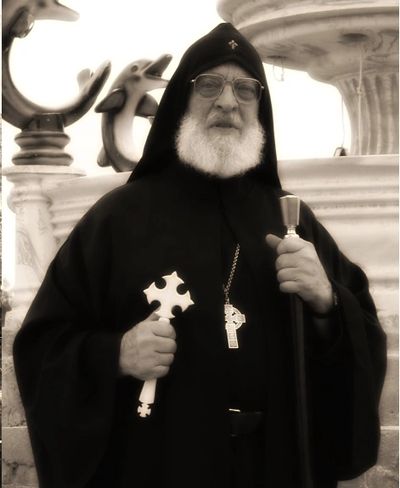Religious leader in traditional black robe holding a cross and staff.