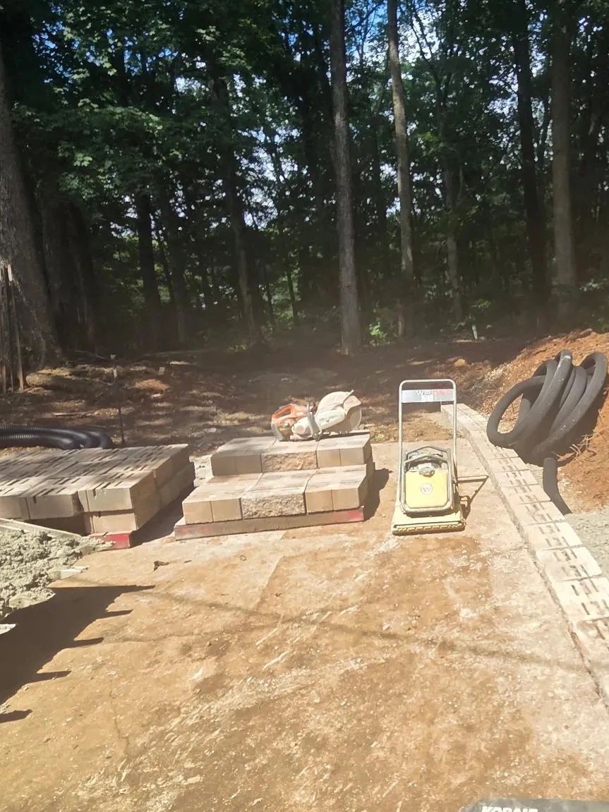 Construction site with paving materials and equipment in a wooded area.