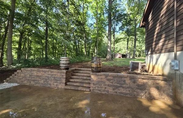 Stone steps with wooden barrels beside a house in a wooded area.