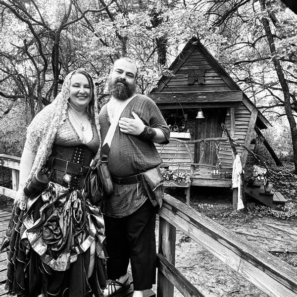 Couple in vintage costumes by rustic wooden cabin.