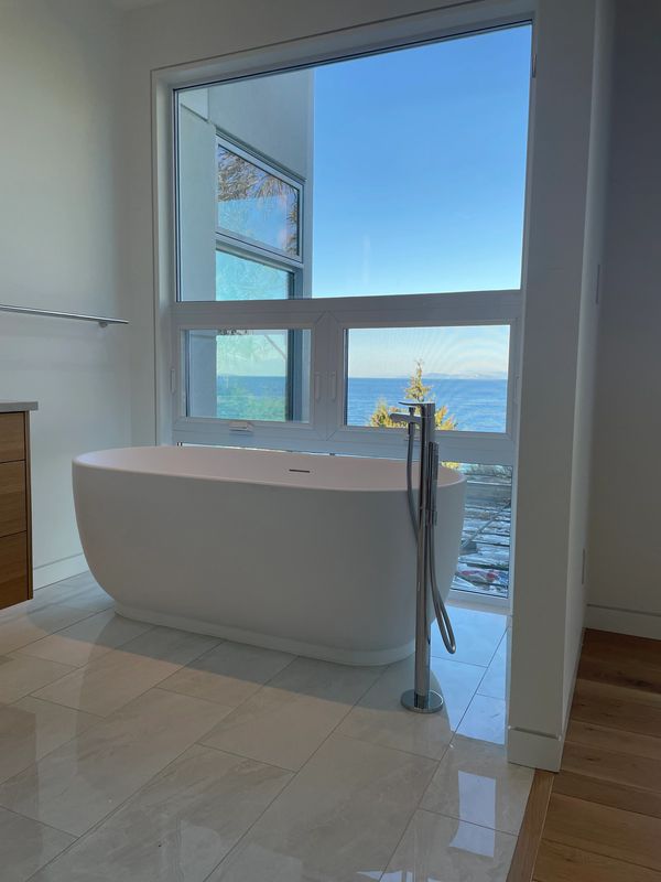 Modern bathroom with a freestanding tub and ocean view through large windows.