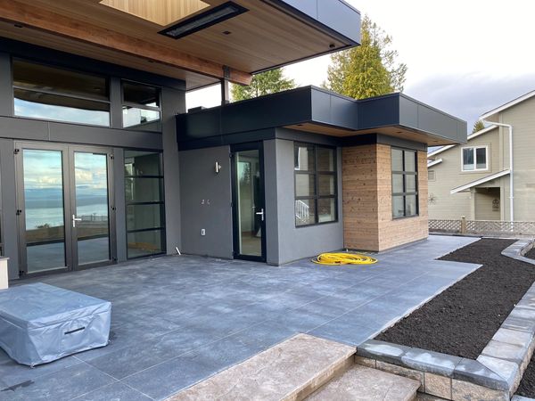 Modern patio with stone tiles, wooden accents, and ocean view through glass doors.
