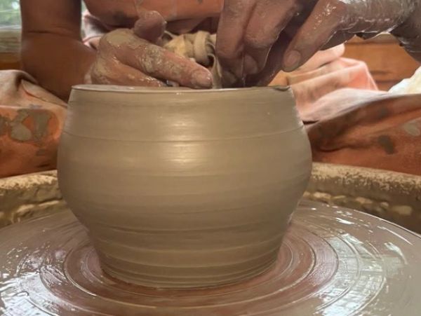 Hands shaping a pot on a pottery wheel.