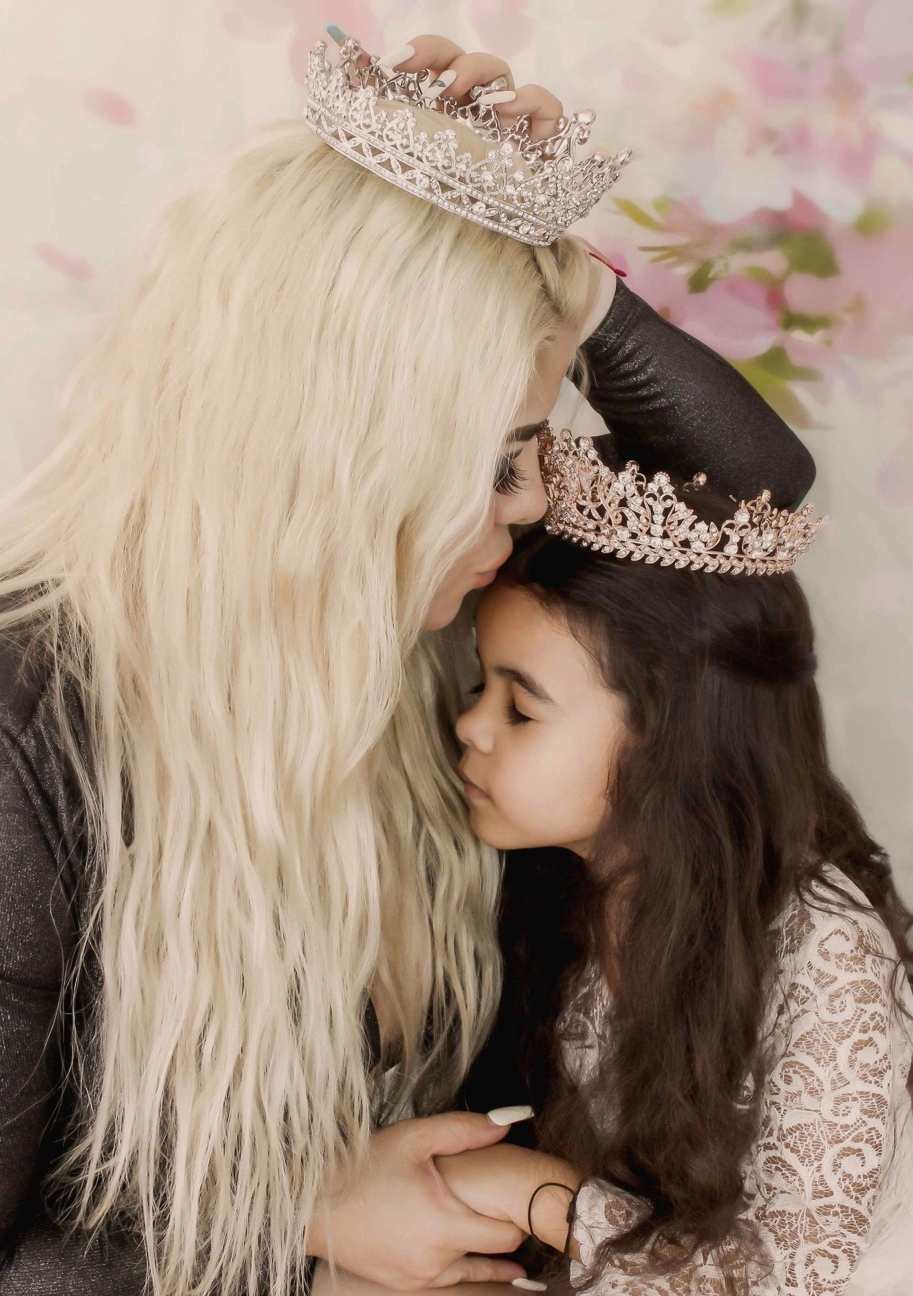 A woman tenderly kisses a young girl wearing crowns, sharing a loving moment.
