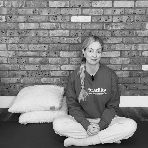 Woman sitting cross-legged on a mat in front of a brick wall.