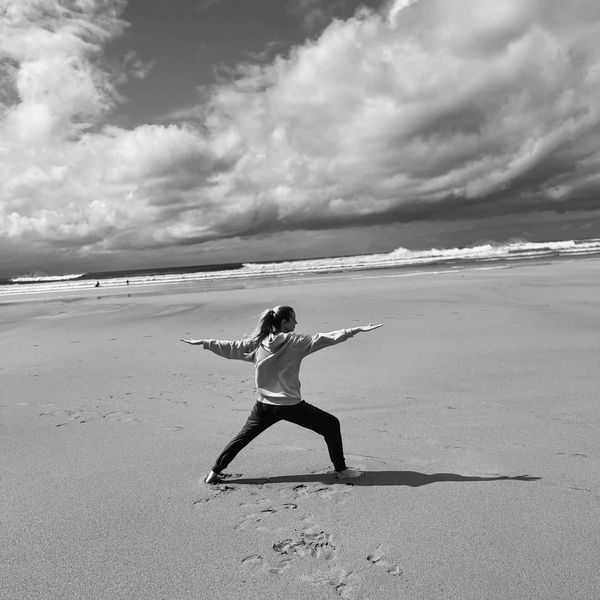 Person practicing yoga on a sandy beach under a cloudy sky.