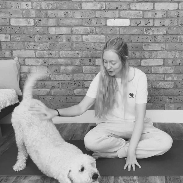 Woman playing and stretching with her dog indoors on a yoga mat.