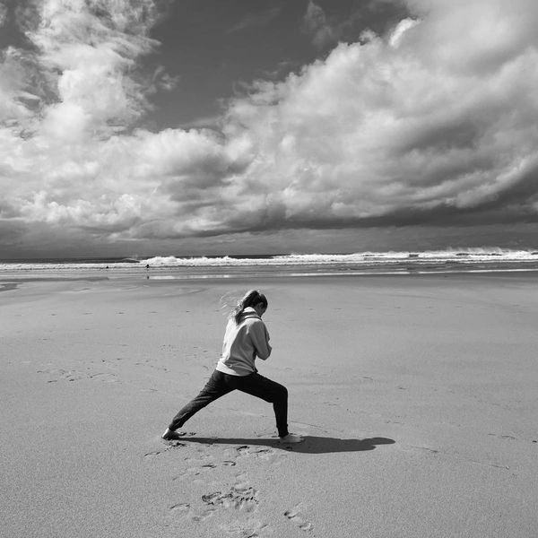 A person practicing a pose on a vast beach under dramatic clouds.