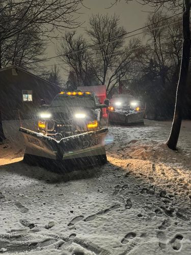 Two snow plows plowing in a storm at night. 