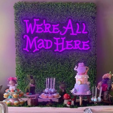 A whimsical dessert table with a neon sign reading 'We're All Mad Here'.