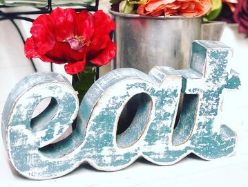 Rustic wooden sign spelling 'eat' with a red flower in the background.
