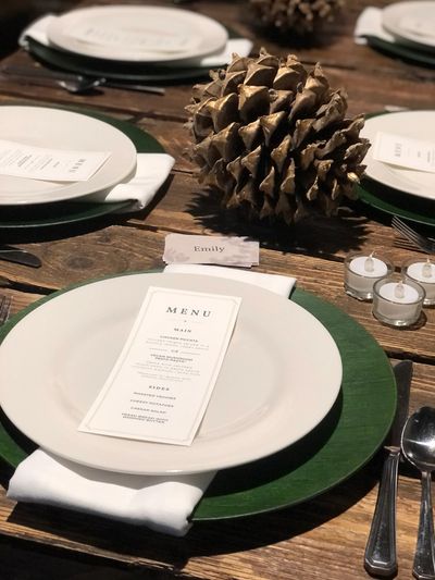 white plate on green charger, on raw wood table. pinecone decoration.
copyright Century Decor Studio