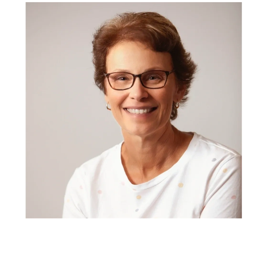 Smiling woman with glasses in a white shirt against a neutral background.