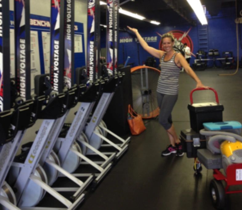A woman poses happily in a gym with rowing machines and equipment.