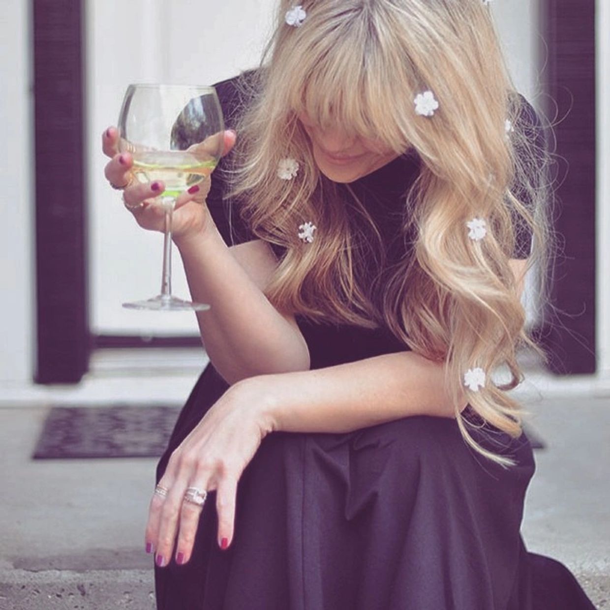 Woman with blonde hair and flowers holds a wine glass, looking down.