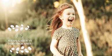 A joyful young girl laughing outdoors in a sunny, natural setting.