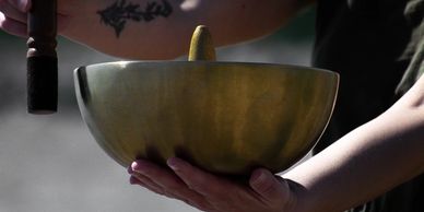 Person holding a brass singing bowl and wooden mallet.
