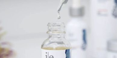 A dropper dispensing liquid into a skincare bottle labeled 'ile'.