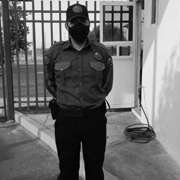 A masked security guard standing outside near a gate.
