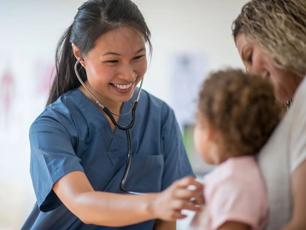 Smiling doctor in blue scrubs examining a young child.