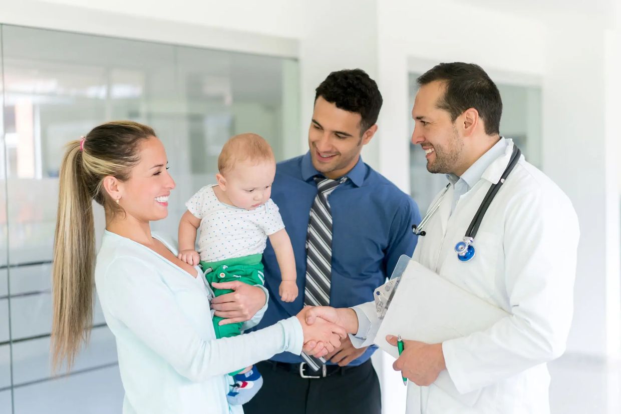 Woman holding baby shaking hands with doctor in white coat.